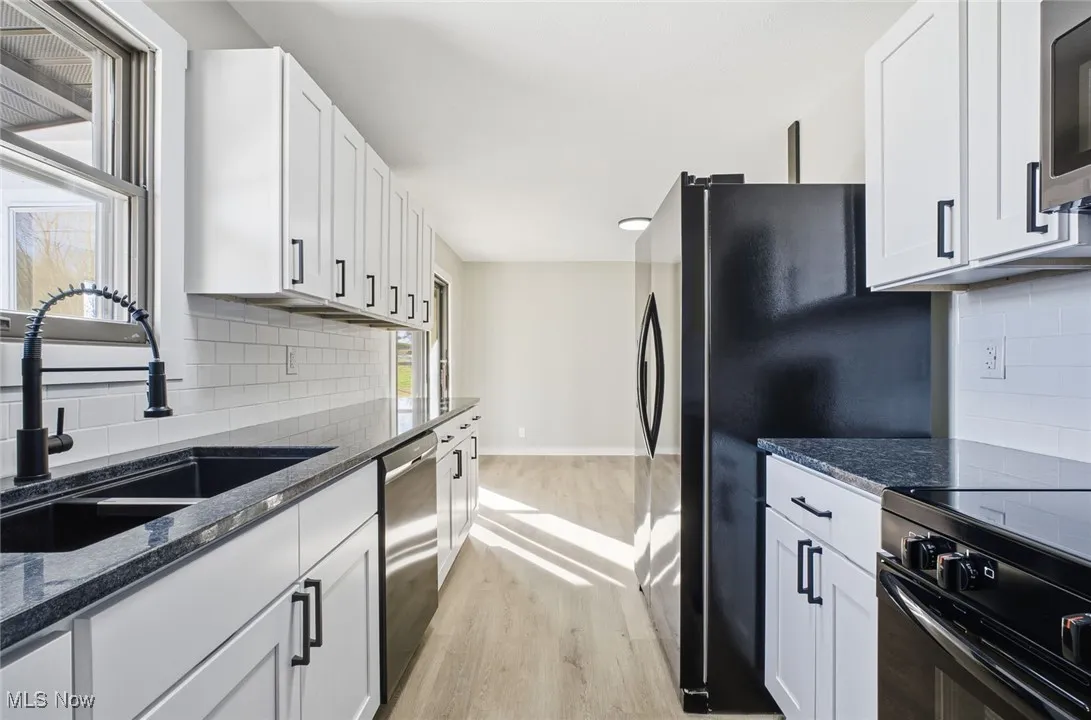 Kitchen featuring tasteful backsplash, dark stone countertops, light wood-type flooring, and white cabinetry