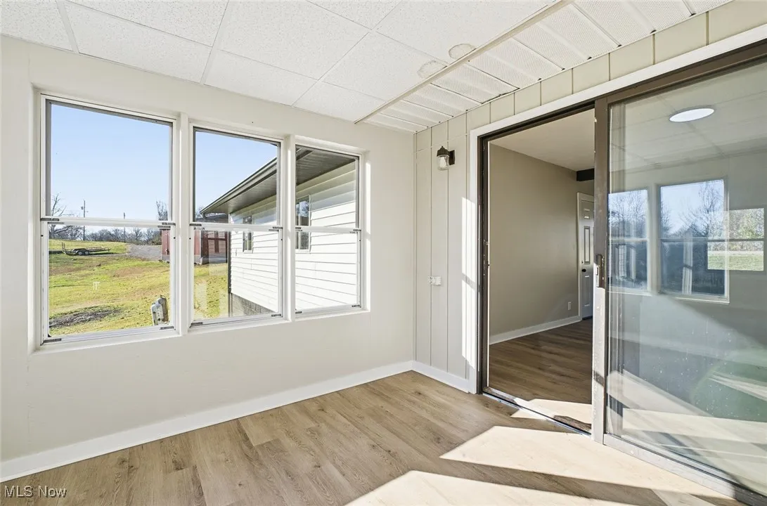 Unfurnished sunroom with wood finished floors, healthy amount of natural light, and a paneled ceiling