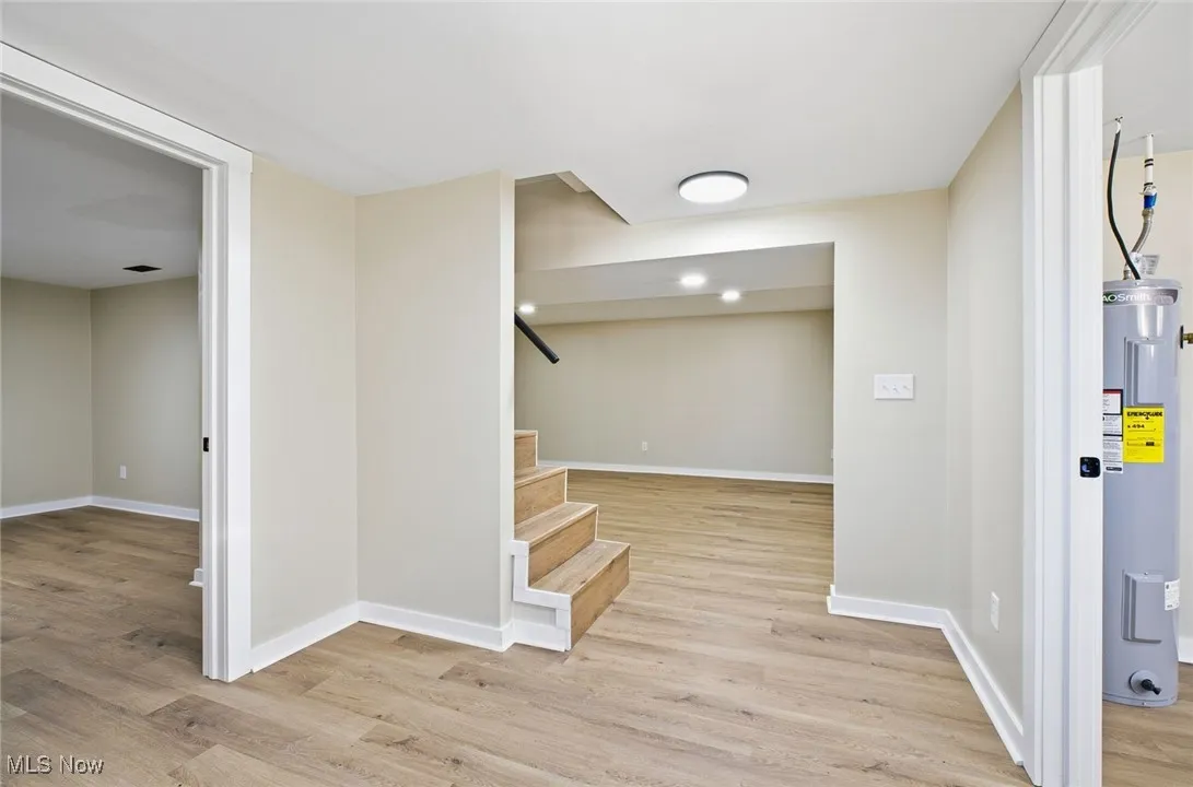 Below grade area featuring light wood-type flooring, water heater, and stairs