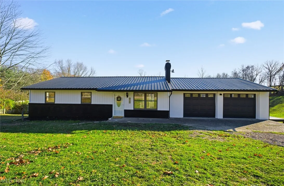 View of front of house featuring a garage, a front lawn, driveway, a metal roof, and board and batten siding