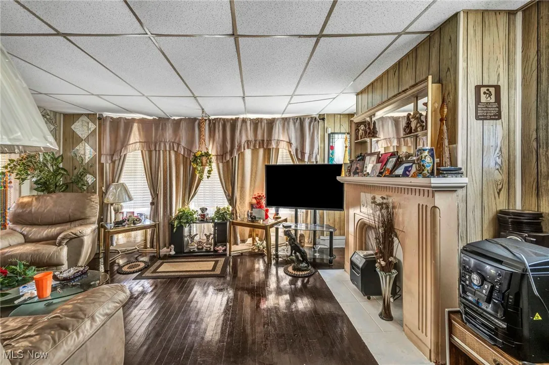 Living area with a drop ceiling, wood walls, a wood stove, and hardwood / wood-style floors