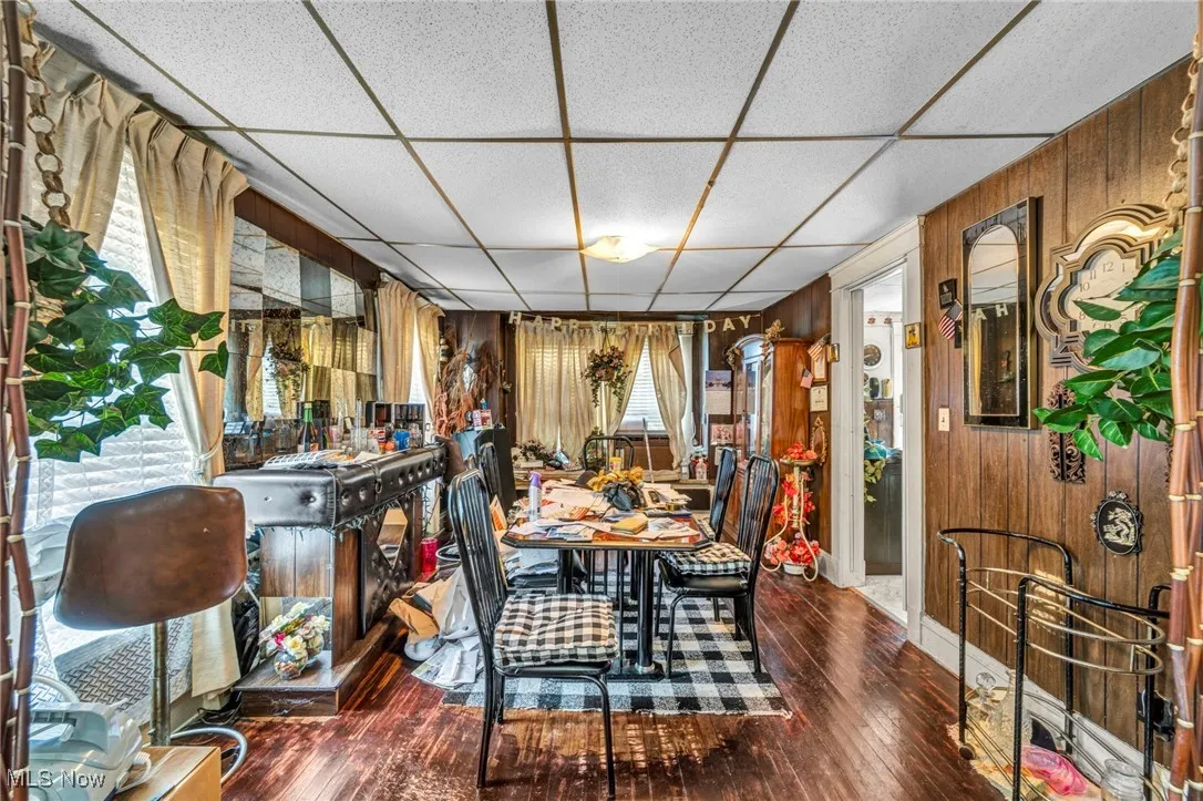 Dining area featuring wood walls, a drop ceiling, and dark wood-type flooring