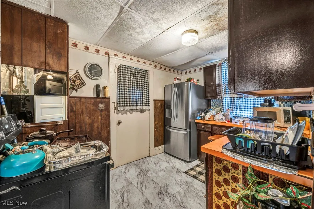 Kitchen featuring appliances with stainless steel finishes, dark brown cabinetry, a paneled ceiling, and wooden counters