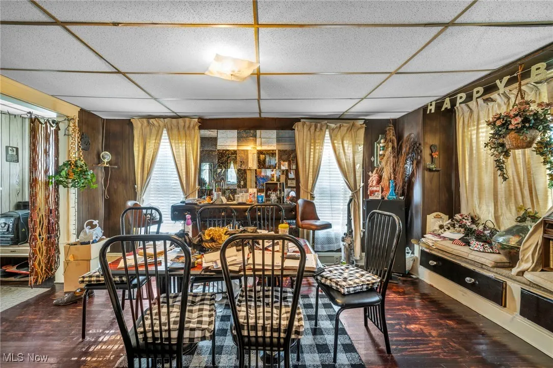 Dining space with wood walls, dark wood-type flooring, and a drop ceiling