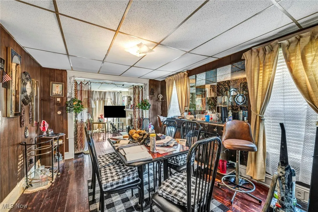 Dining room with wooden walls, a paneled ceiling, and dark wood-type flooring