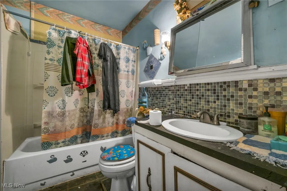 Bathroom featuring shower / tub combo with curtain, decorative backsplash, and vanity