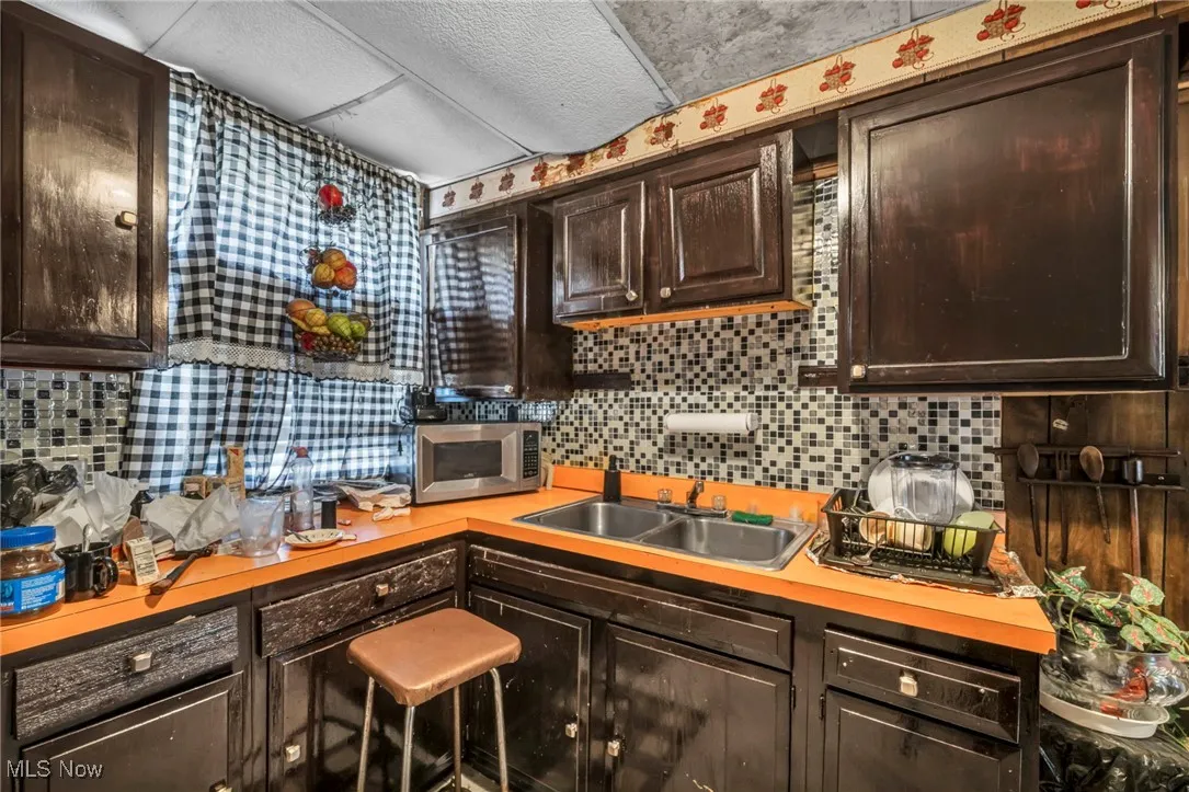 Kitchen with dark brown cabinetry, backsplash, stainless steel microwave, and light countertops