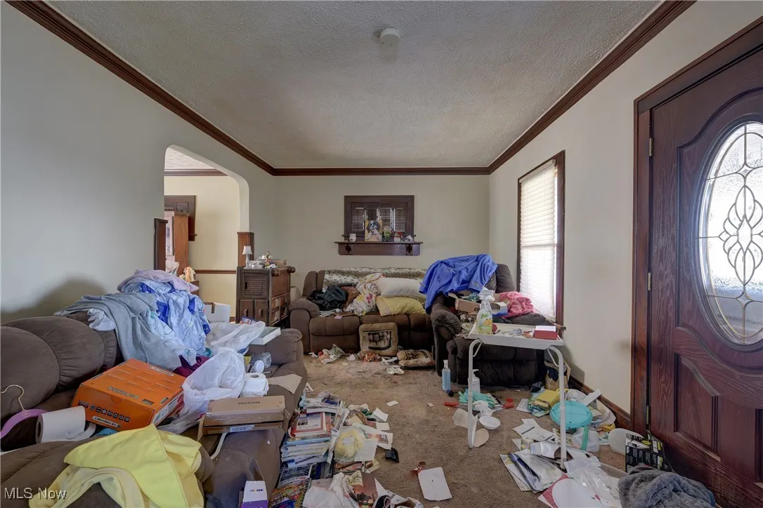 Entryway with a textured ceiling, arched walkways, ornamental molding, and carpet flooring