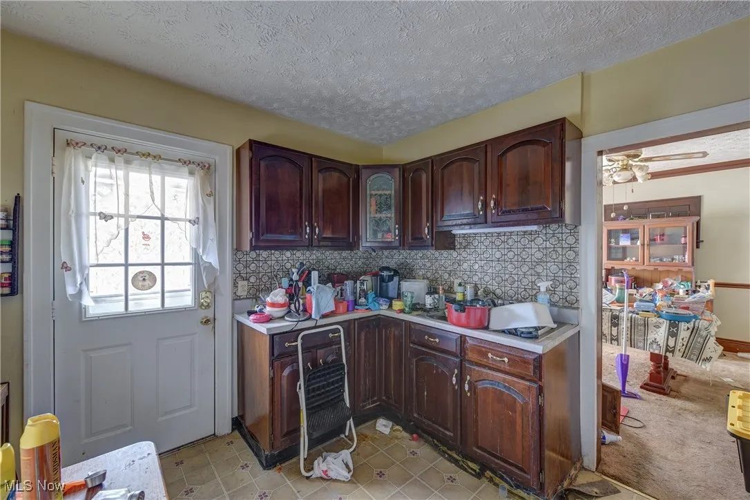 Kitchen featuring decorative backsplash, light countertops, a textured ceiling, ceiling fan, and dark brown cabinetry