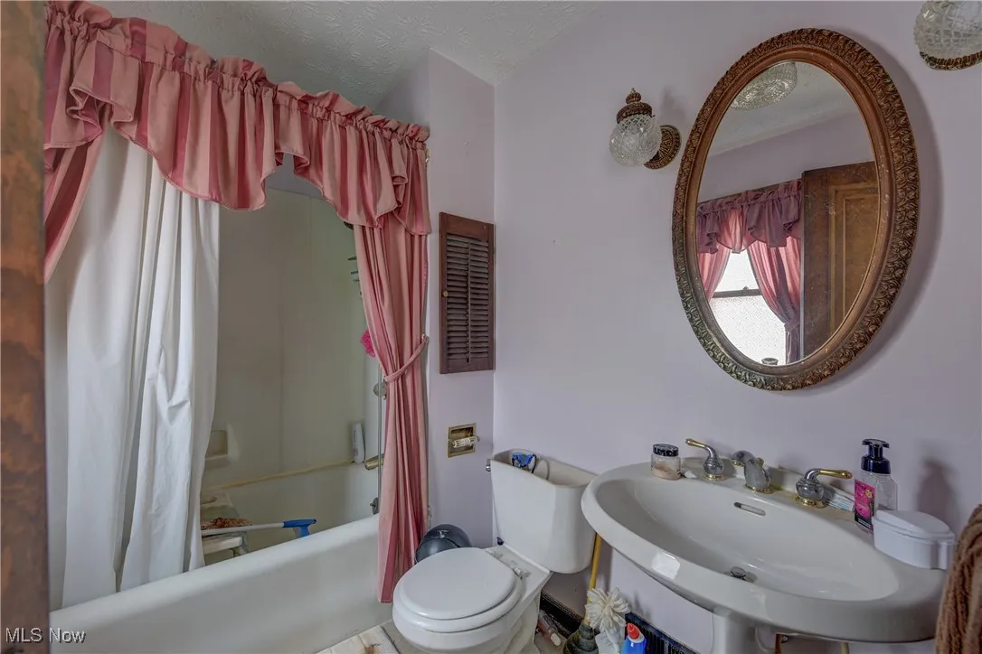 Full bathroom featuring shower / bath combination with curtain and a textured ceiling