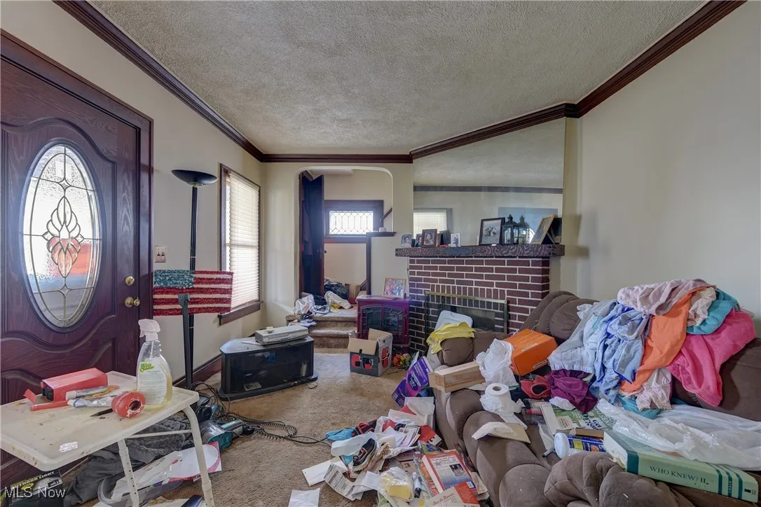 Carpeted living room featuring ornamental molding, a textured ceiling, and a brick fireplace