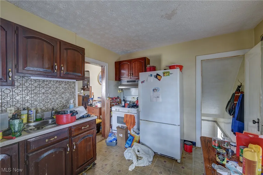Kitchen featuring a textured ceiling, white appliances, light countertops, decorative backsplash, and light tile patterned floors