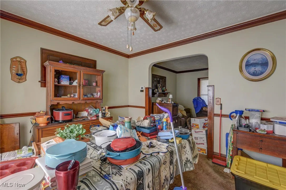 Dining space with crown molding, a textured ceiling, dark carpet, arched walkways, and ceiling fan