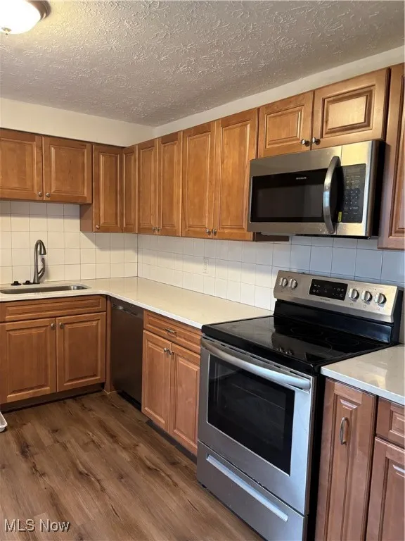 Kitchen with stainless steel appliances, brown cabinets, backsplash, dark wood finished floors, and a textured ceiling