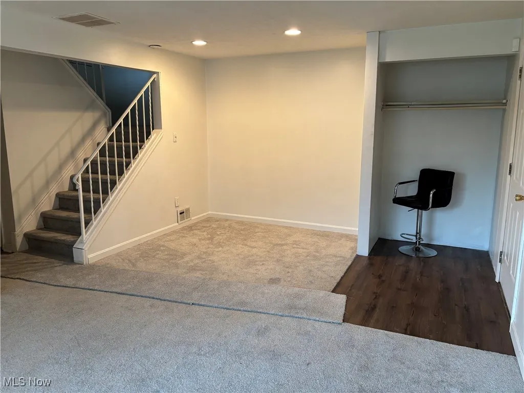 Living and dining room with recessed lighting, dark colored carpet, stairs, and dark wood finished floors