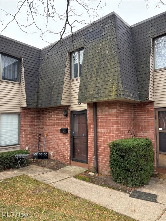 Doorway to property with mansard roof, brick siding, and roof with shingles