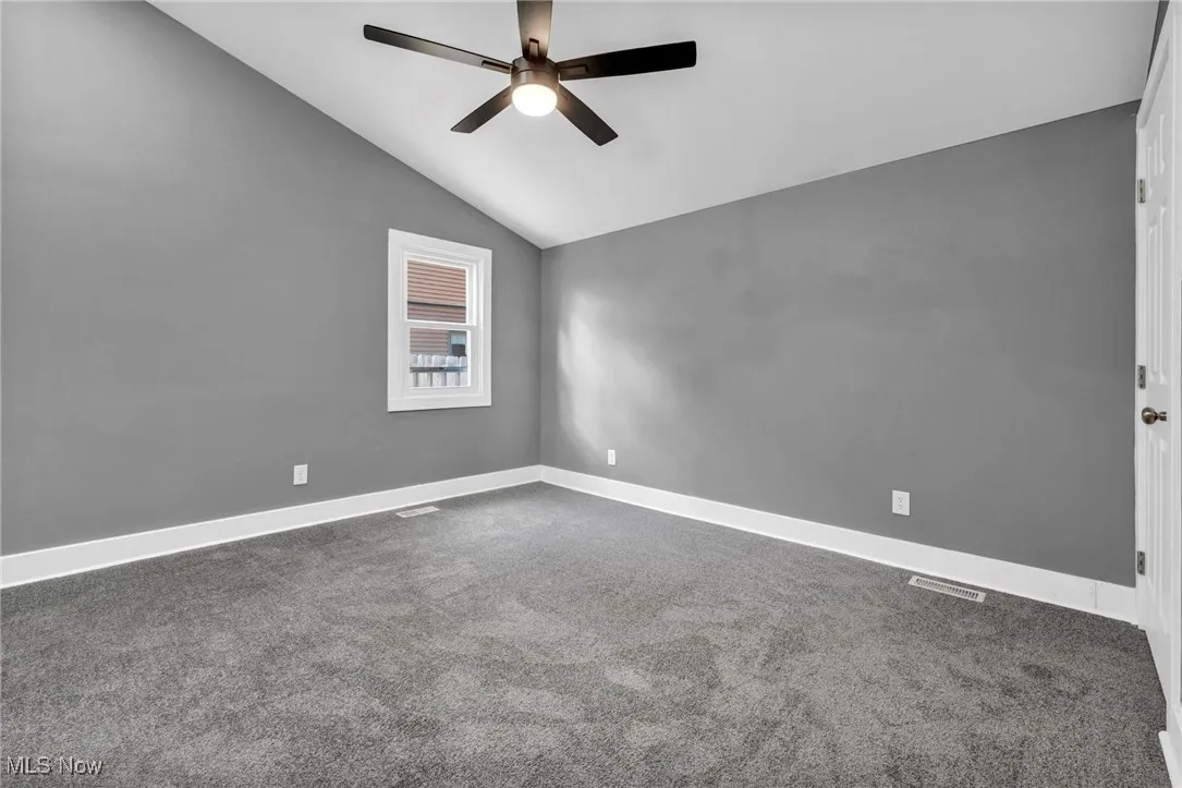 Carpeted spare room featuring lofted ceiling and ceiling fan
