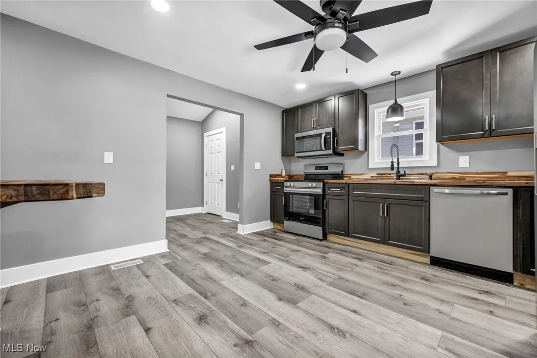 Kitchen featuring appliances with stainless steel finishes, butcher block counters, light wood-style floors, a ceiling fan, and decorative light fixtures