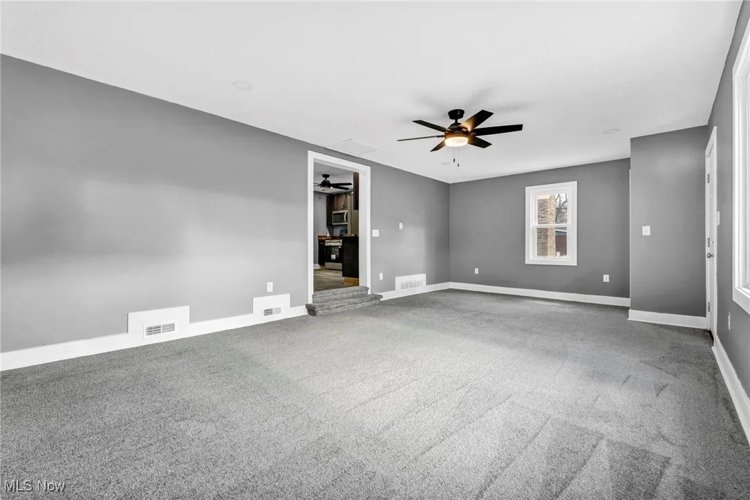 Carpeted spare room with a ceiling fan and baseboards