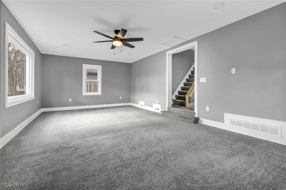 Carpeted empty room featuring stairs, healthy amount of natural light, and a ceiling fan