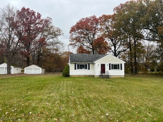 Bungalow-style home with a detached garage, a front lawn, entry steps, an outbuilding, and view of scattered trees