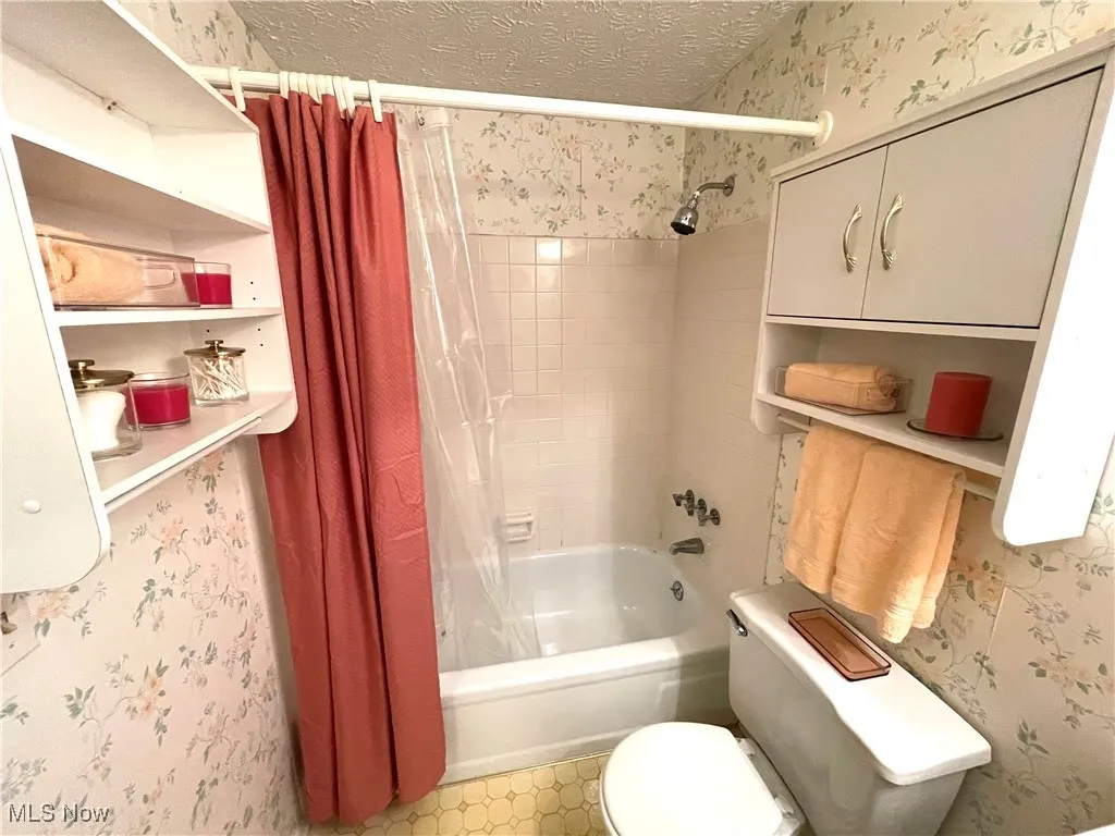 Full bath with wallpapered walls, shower / tub combo, and a textured ceiling