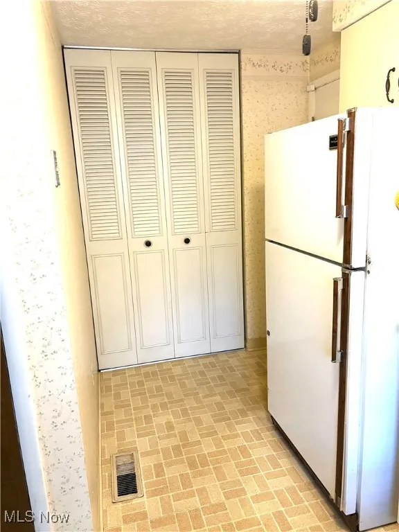 Kitchen with freestanding refrigerator, brick patterned floors, a textured ceiling, and wallpapered walls