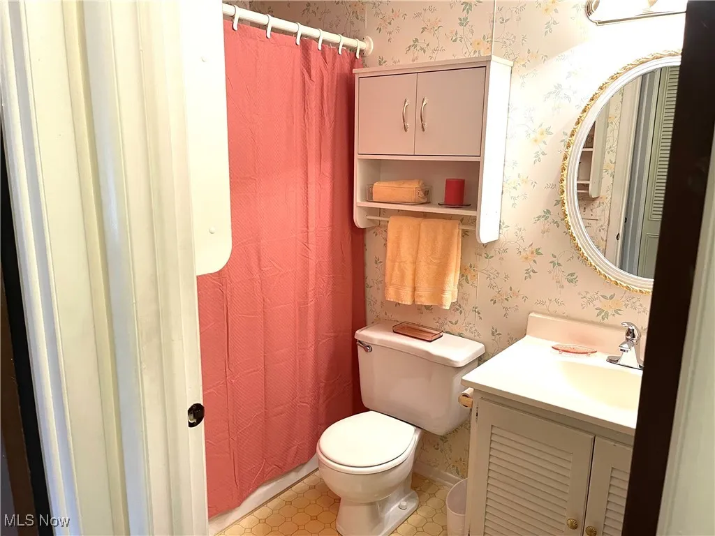 Bathroom with wallpapered walls, a shower with curtain, and vanity