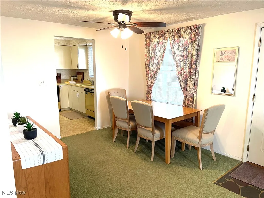 Dining room with a textured ceiling, light colored carpet, and a ceiling fan
