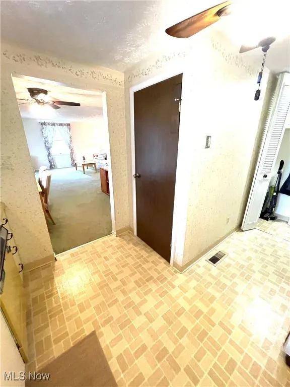 Corridor with brick patterned floors, a textured ceiling, and wallpapered walls