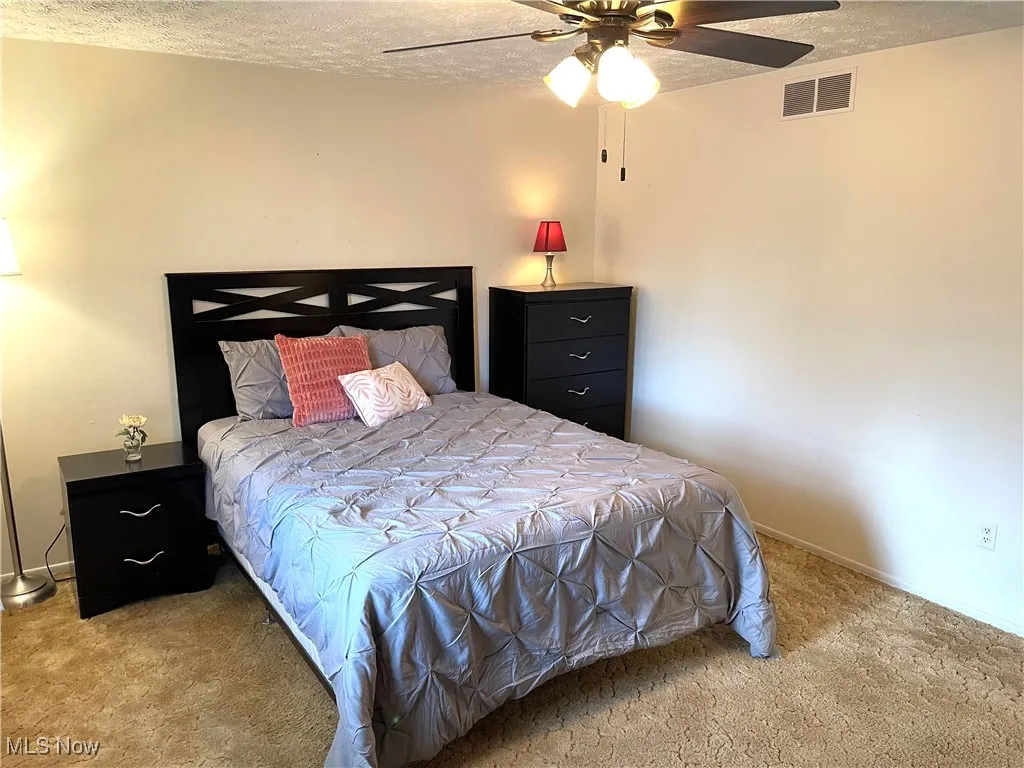 Bedroom with a textured ceiling, carpet floors, and ceiling fan