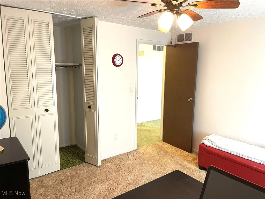 Bedroom featuring a textured ceiling, light carpet, a closet, and a ceiling fan