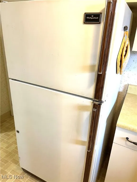 Kitchen view of freestanding refrigerator, light countertops, wallpapered walls, and white cabinetry