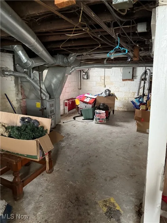 Unfinished basement featuring electric panel and heating unit
