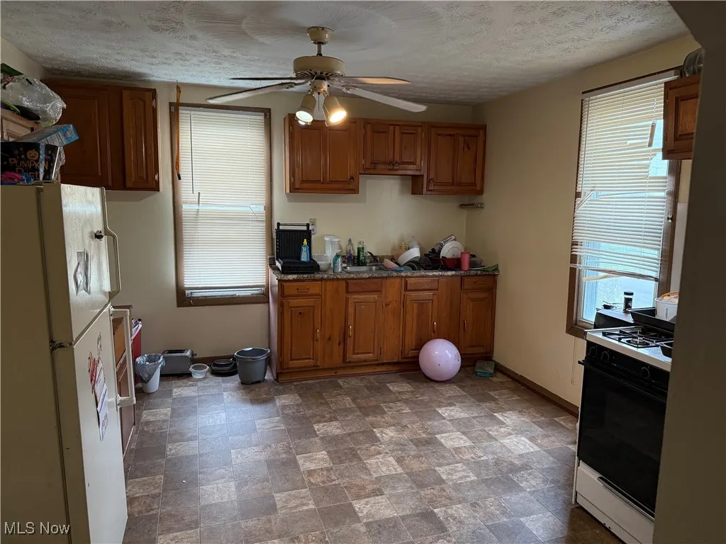 Kitchen with stone finish floors, freestanding refrigerator, gas range, brown cabinets, and a textured ceiling