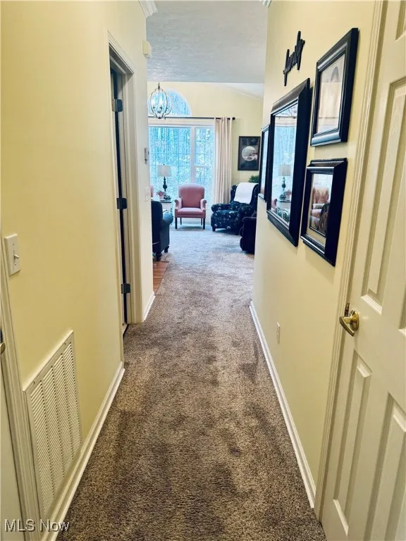Hall featuring carpet flooring and a chandelier