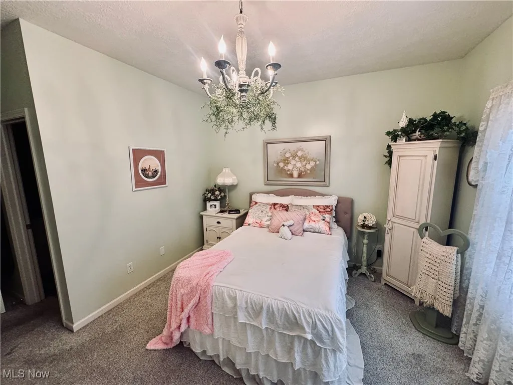 Carpeted bedroom featuring a chandelier and a textured ceiling