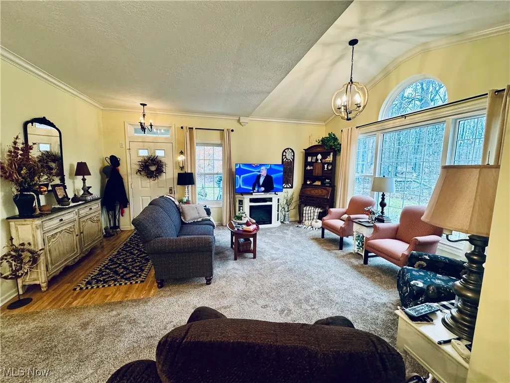 Carpeted living room featuring a chandelier, crown molding, healthy amount of natural light, lofted ceiling, and a textured ceiling