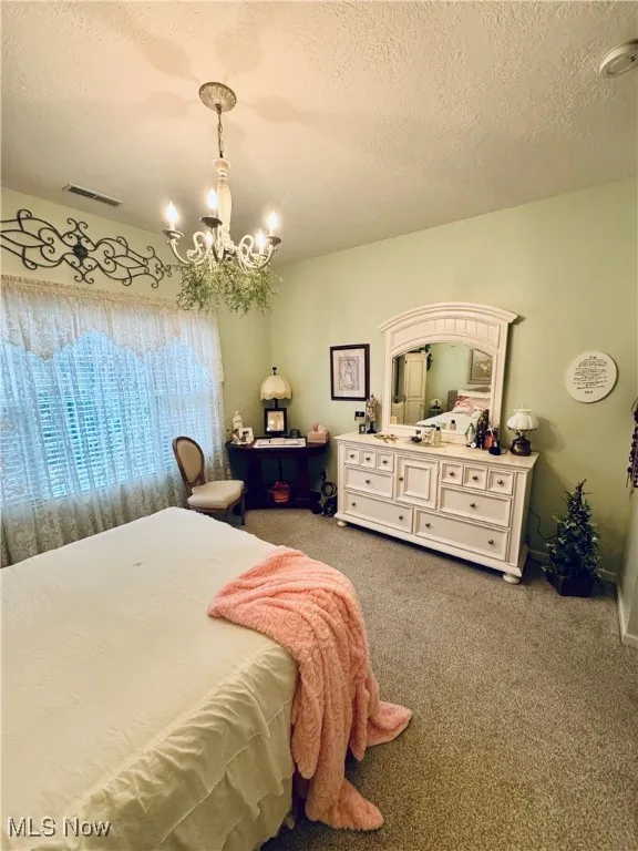 Bedroom with a textured ceiling, light colored carpet, and a chandelier