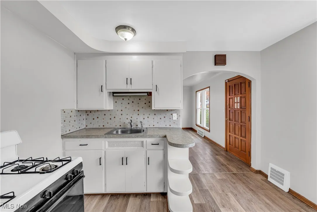 Kitchen with gas range gas stove, arched walkways, white cabinets, tasteful backsplash, and light countertops