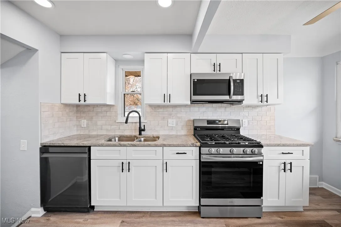 Kitchen featuring white cabinets, stainless steel appliances, decorative backsplash, light stone counters, and recessed lighting