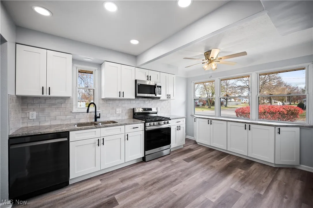 Kitchen featuring appliances with stainless steel finishes, white cabinets, decorative backsplash, light stone counters, and dark wood-style floors