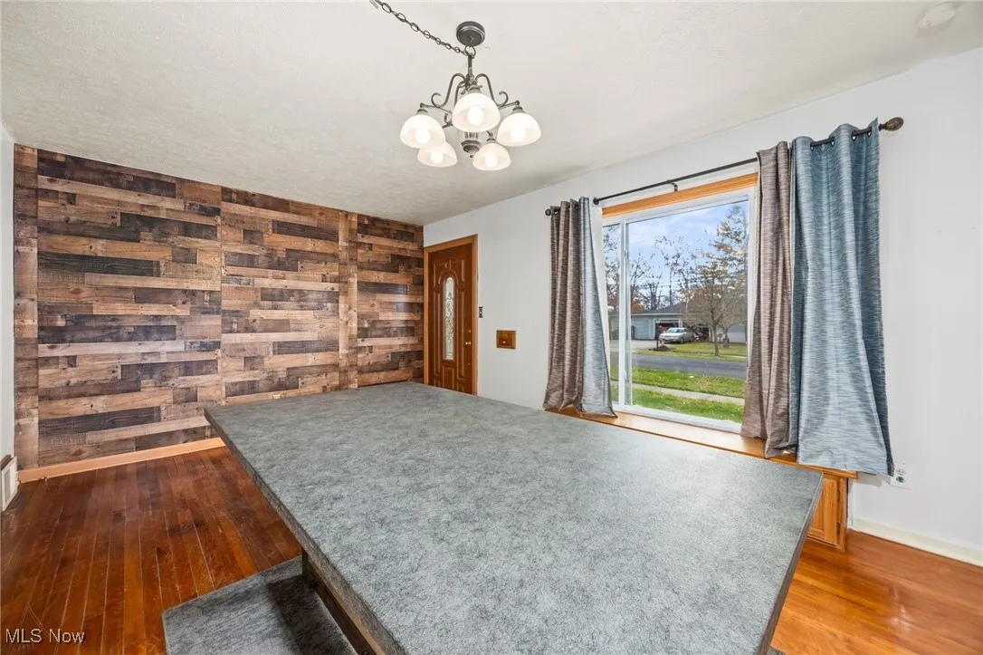 Dining room featuring wood walls, dark wood finished floors, a chandelier, and a textured ceiling
