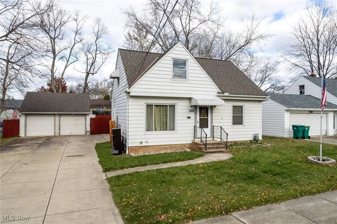 View of front of property featuring an outbuilding, a detached garage, a front lawn, and roof with shingles