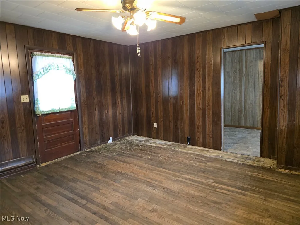 Spare room featuring a ceiling fan, dark wood-type flooring, and wood walls