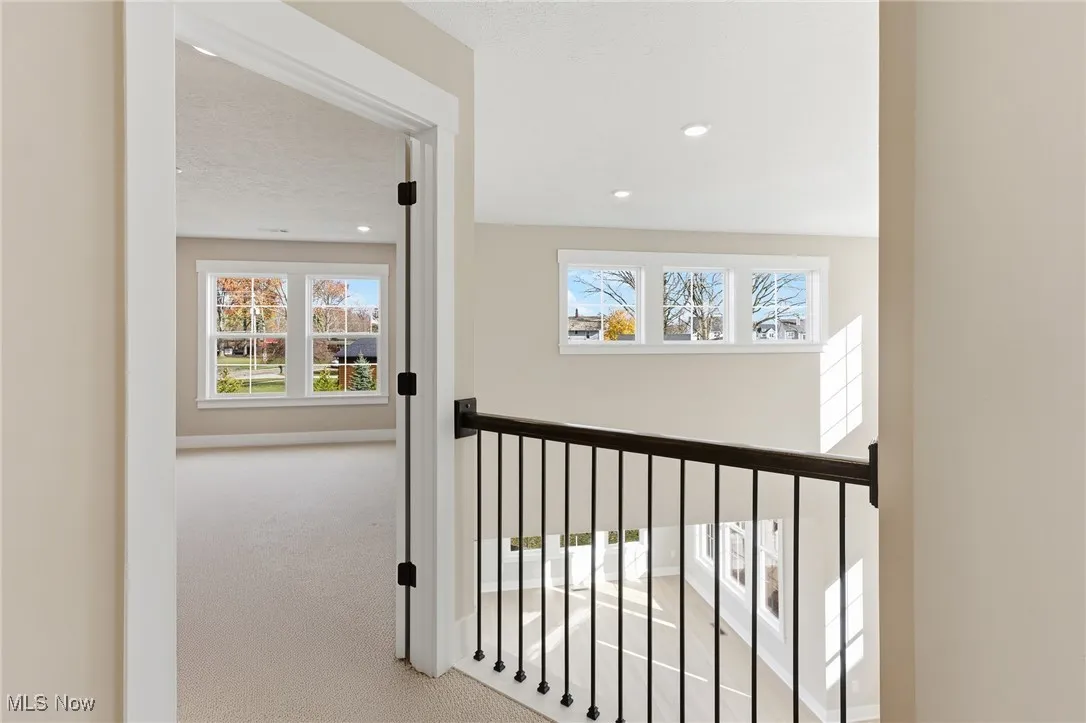 Upstairs hallway overlooking the main flooe with carpet flooring and recessed lighting