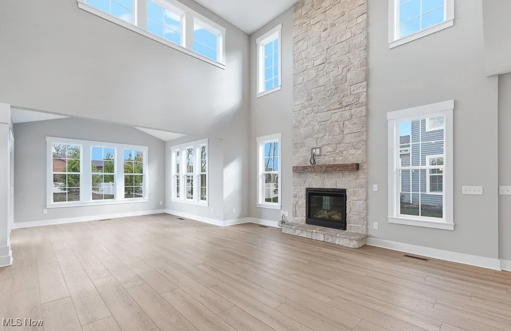 Unfurnished living room with light wood-type flooring, a stone fireplace, and a towering ceiling