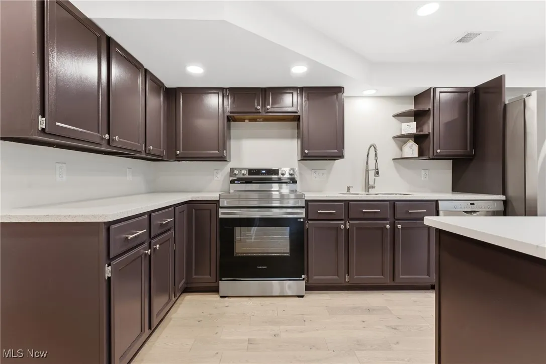 Kitchen featuring stainless steel appliances, open shelves, dark brown cabinets, recessed lighting, and light wood-type flooring