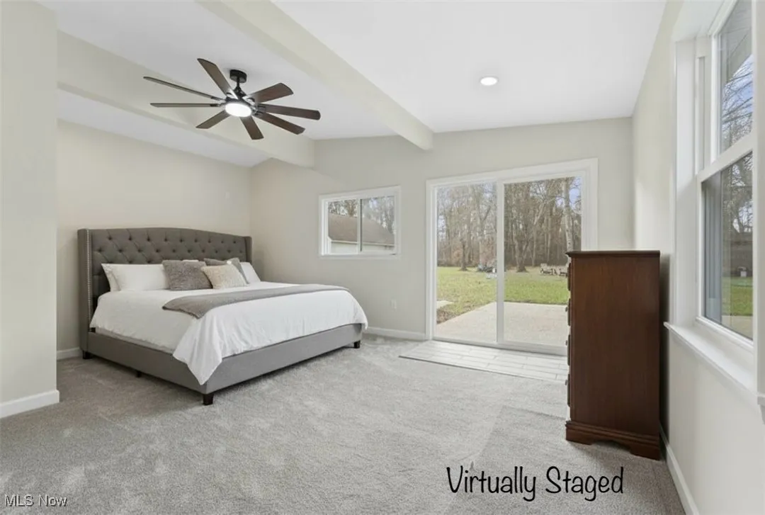 Bedroom featuring multiple windows, beamed ceiling, light carpet, access to outside, and a ceiling fan