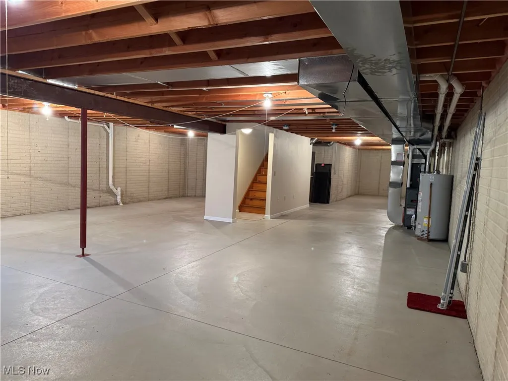 Unfinished below grade area featuring stairway, water heater, and heating unit